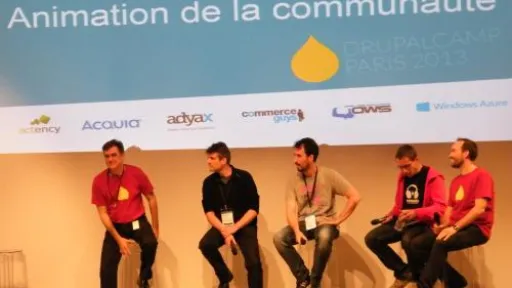 Cinq hommes assis sur scène à une conférence DrupalCamp.