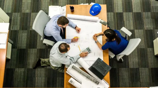 Assistance à Maîtrise d’Ouvrage internet avec trois personnes autour de plans d'architecte sur une table.